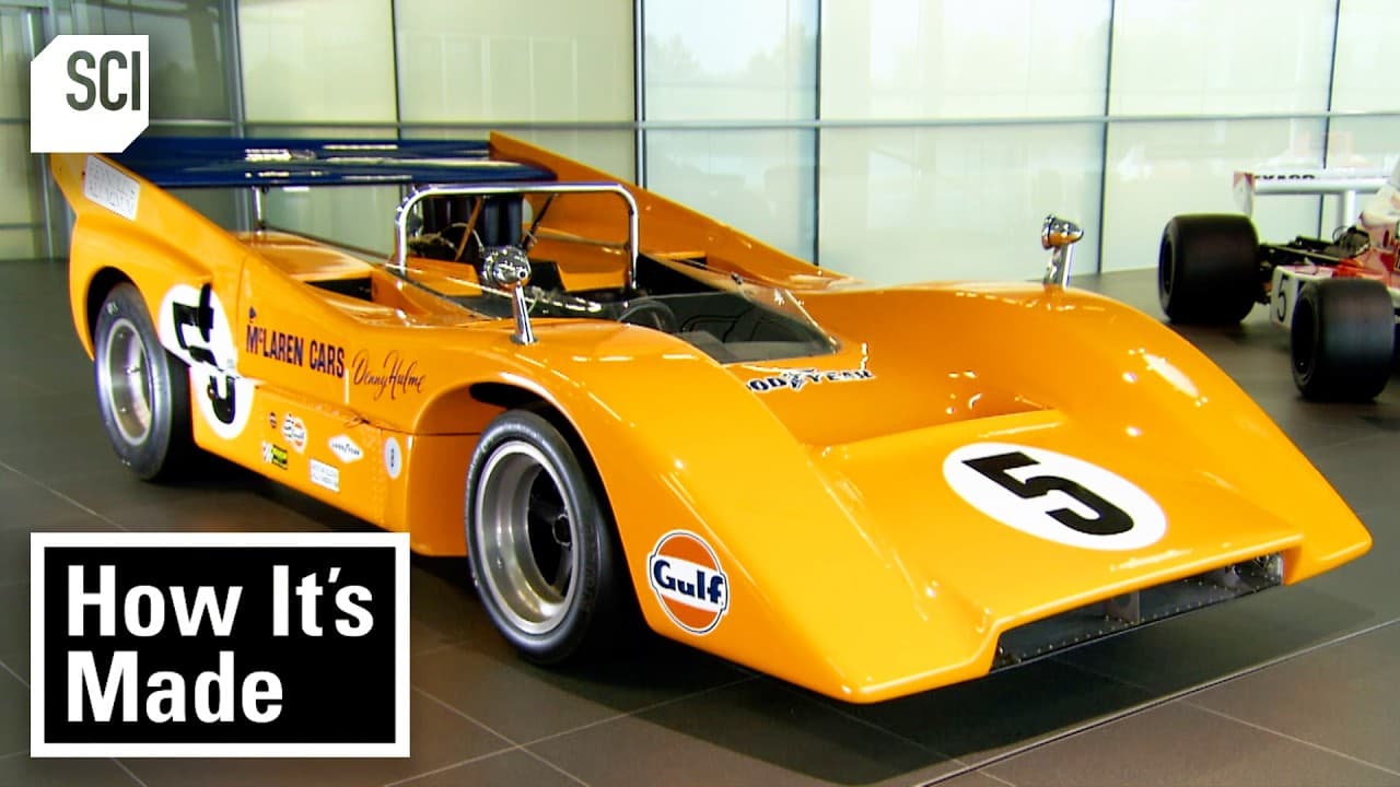 Bright orange McLaren race car with number 5 displayed in a modern showroom with SCI and "How It's Made" branding visible