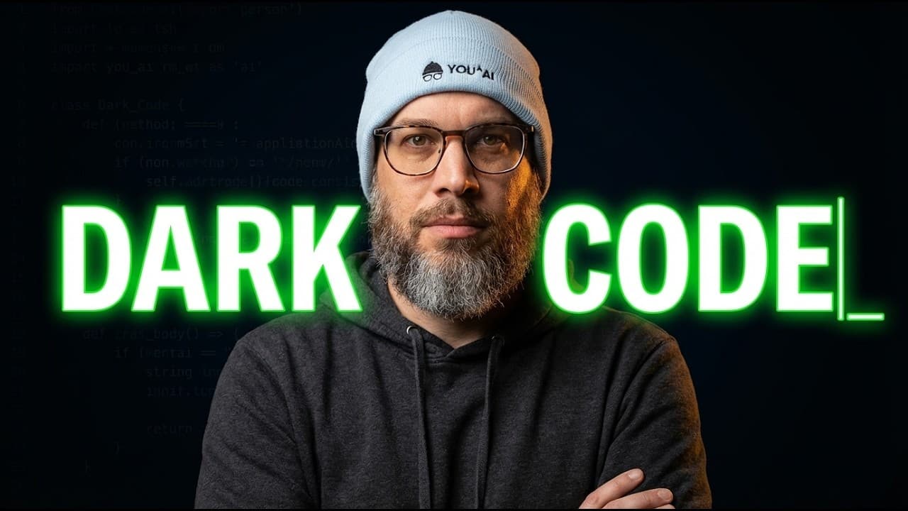 A bearded man wearing glasses and a light gray beanie stands against a dark background with bright green neon text reading…