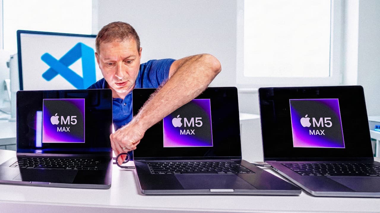 Man in blue shirt examines three MacBook laptops displaying M5 Max chip logos on their screens with Visual Studio Code logo…