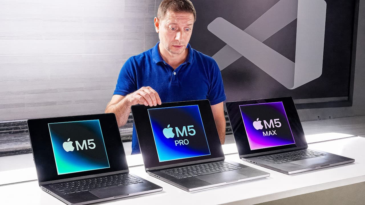 Man in blue shirt examining three MacBook Pro laptops displaying M5, M5 Pro, and M5 Max chip logos on their screens.