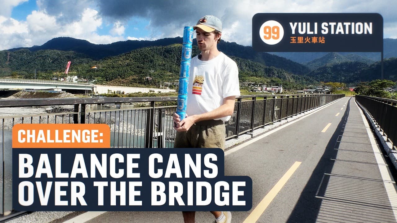 Man balancing stacked blue cans on a bridge at Yuli Station with mountainous landscape and river in background