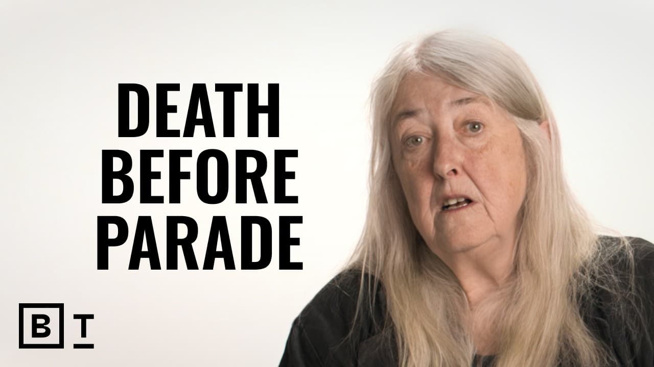 Woman with long grey hair against white background with text "DEATH BEFORE PARADE" and "BT" logo visible