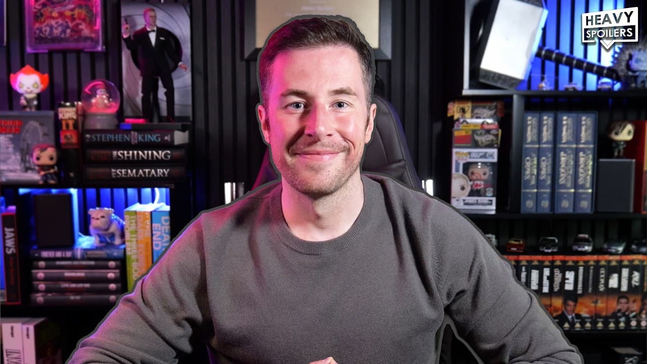 Man in gaming chair smiling at camera in neon-lit room filled with collectibles and Stephen King book collection, with…